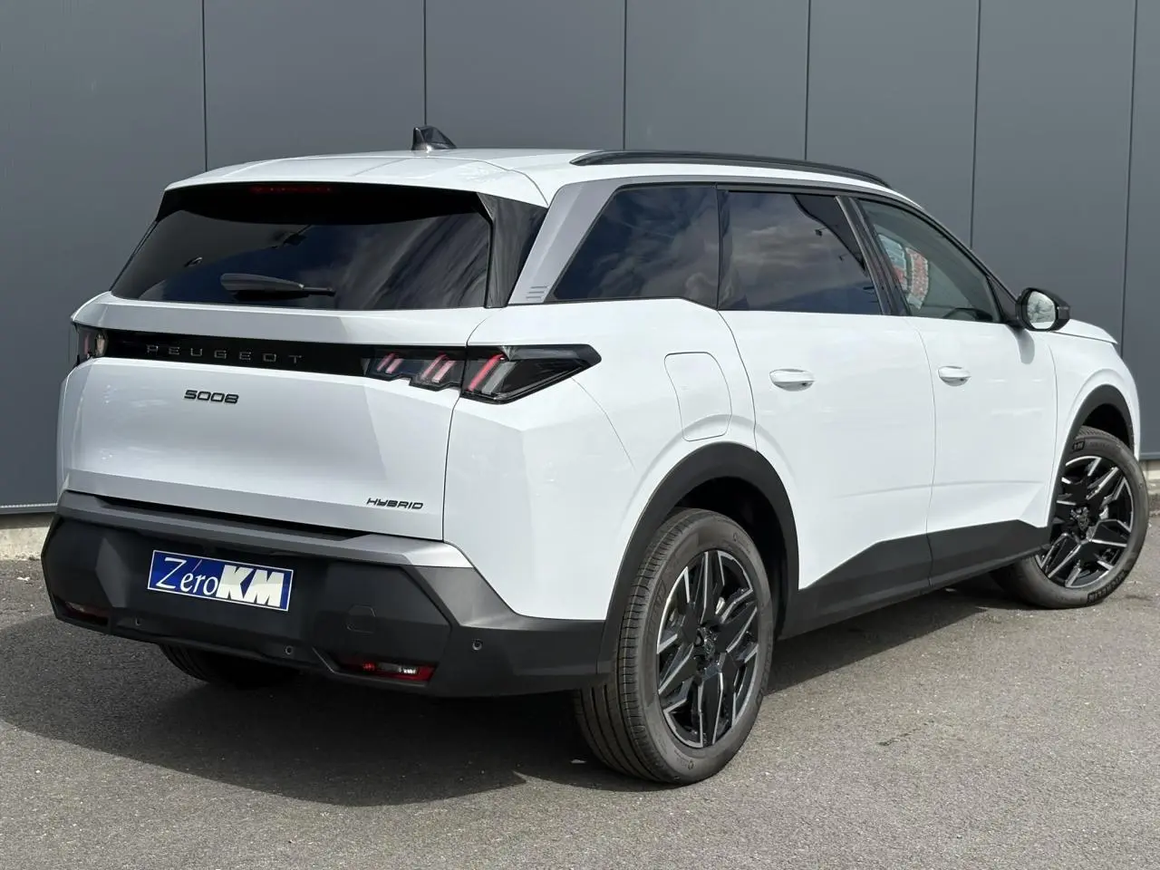 Vue 3/4 arrière droite d'un Peugeot 5008 Hybrid blanc Okénite avec jantes alliage noires et vitres teintées.