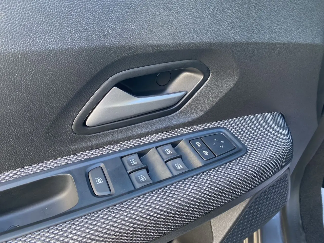 Gros plan sur la commande des vitres électriques côté conducteur avec insert gris texturé dans une Dacia Sandero Stepway 2025.