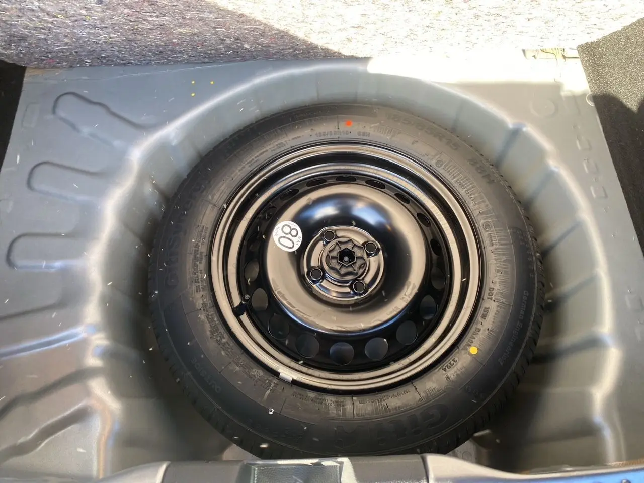 Roue de secours noire dans le coffre d'une Dacia Sandero Stepway 2025, entourée de la carrosserie gris schiste.