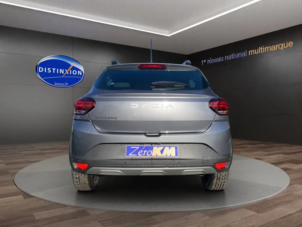 Vue arrière d'une Dacia Sandero Stepway gris schiste avec feux LED et plaque Zero KM en showroom.