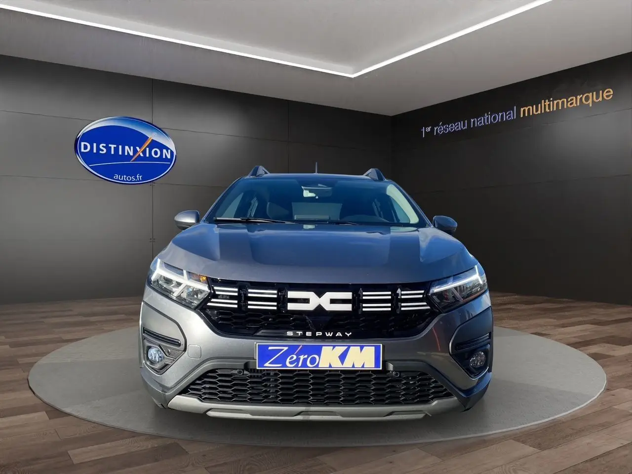 Vue frontale d'une Dacia Sandero Stepway gris schiste avec calandre noire et logo distinctif, en showroom.