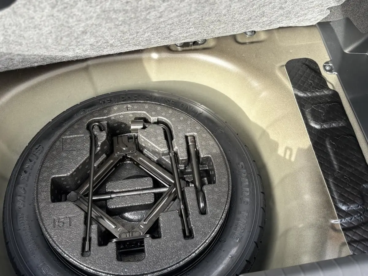 Vue rapprochée de la roue de secours et du cric dans le coffre d'une Hyundai i20 gris clair 2026.