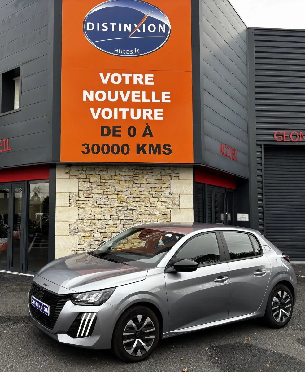 Peugeot 208 gris clair vue de profil droit devant un bâtiment avec panneau orange Distinxion.