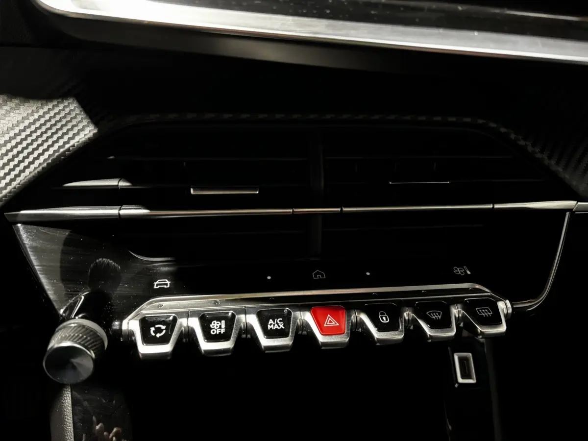 Gros plan sur la rangée de commandes chromées et boutons du tableau de bord noir de la Peugeot 208 gris clair 2024.