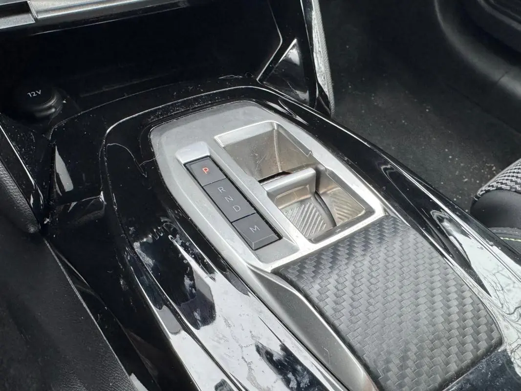 Gros plan sur la console centrale noire brillante de la Peugeot 208 Hybrid 110 e-DCS6 GT avec levier de boîte automatique.