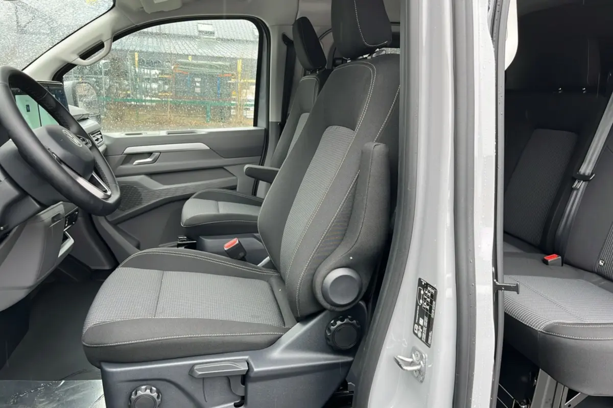 Vue latérale intérieure côté gauche du Volkswagen Transporter Stone Grey 2026, montrant les sièges avant et arrière en tissu gris.