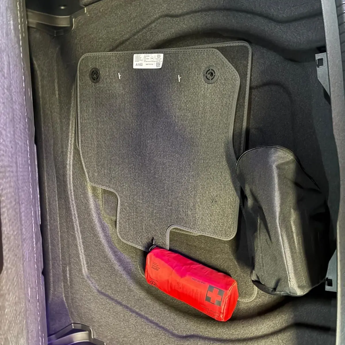 Coffre ouvert vu de dessus d’un Volkswagen Tiguan noir Grenadilla avec tapis de sol et trousse de secours rouge.