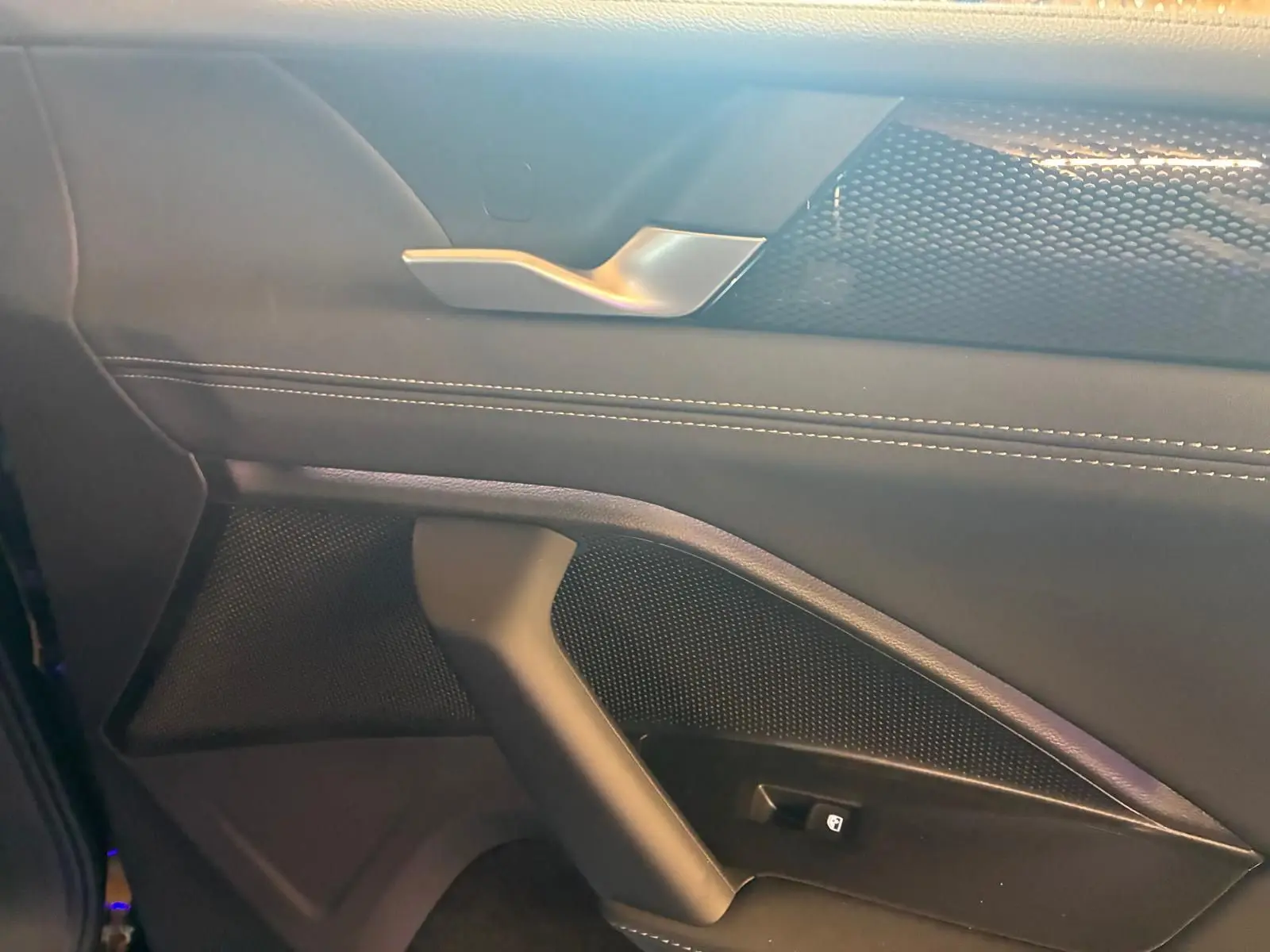 Détail de la porte intérieure côté gauche du Volkswagen Tiguan noir Grenadilla, avec poignée argentée et surpiqûres blanches.