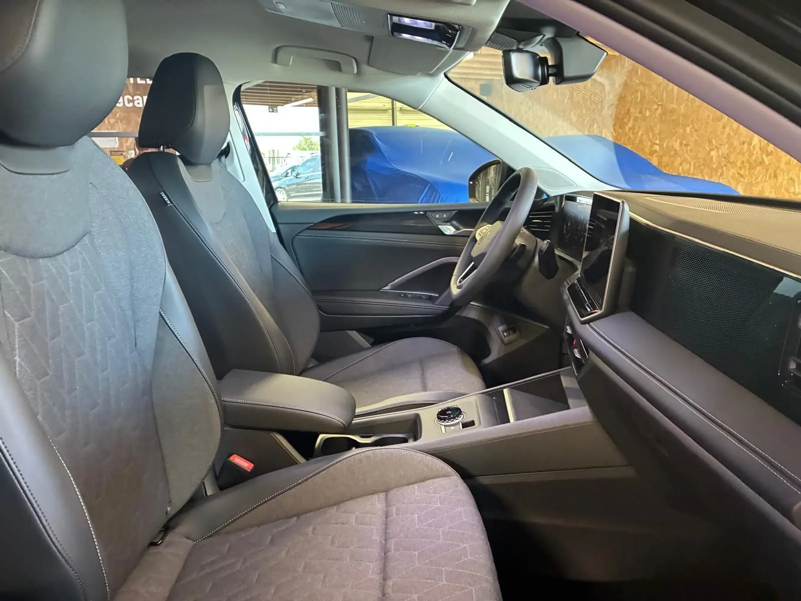 Vue intérieure côté conducteur du Volkswagen Tiguan 2026, sièges tissu gris et tableau de bord moderne avec écran tactile.
