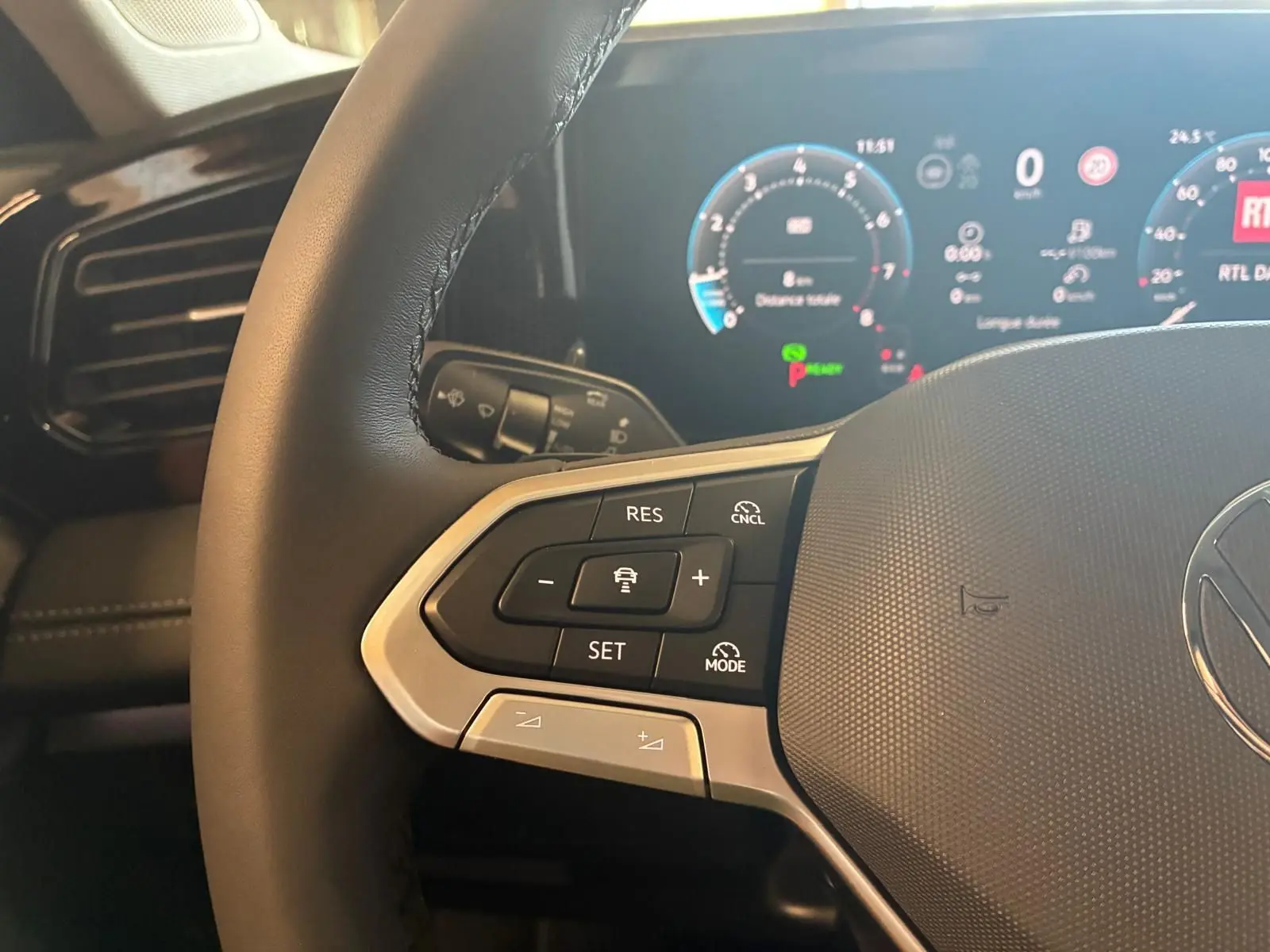 Gros plan sur le volant noir du Volkswagen Tiguan 2026, avec commandes de régulateur et tableau de bord digital en arrière-plan.