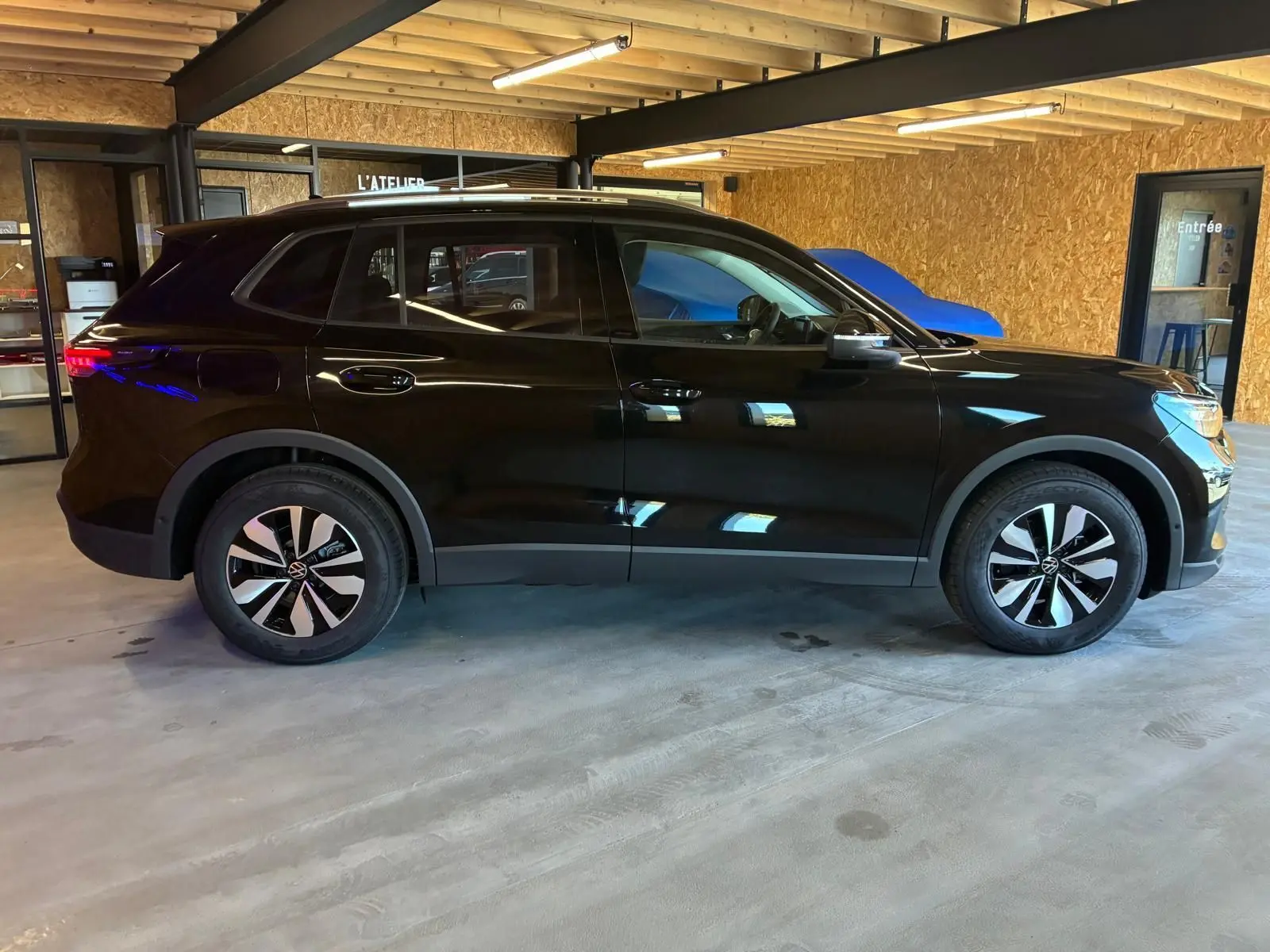 Vue de profil droit d'un Volkswagen Tiguan noir Grenadilla métallisé, avec jantes bi-ton et intérieur visible à travers les vitres.