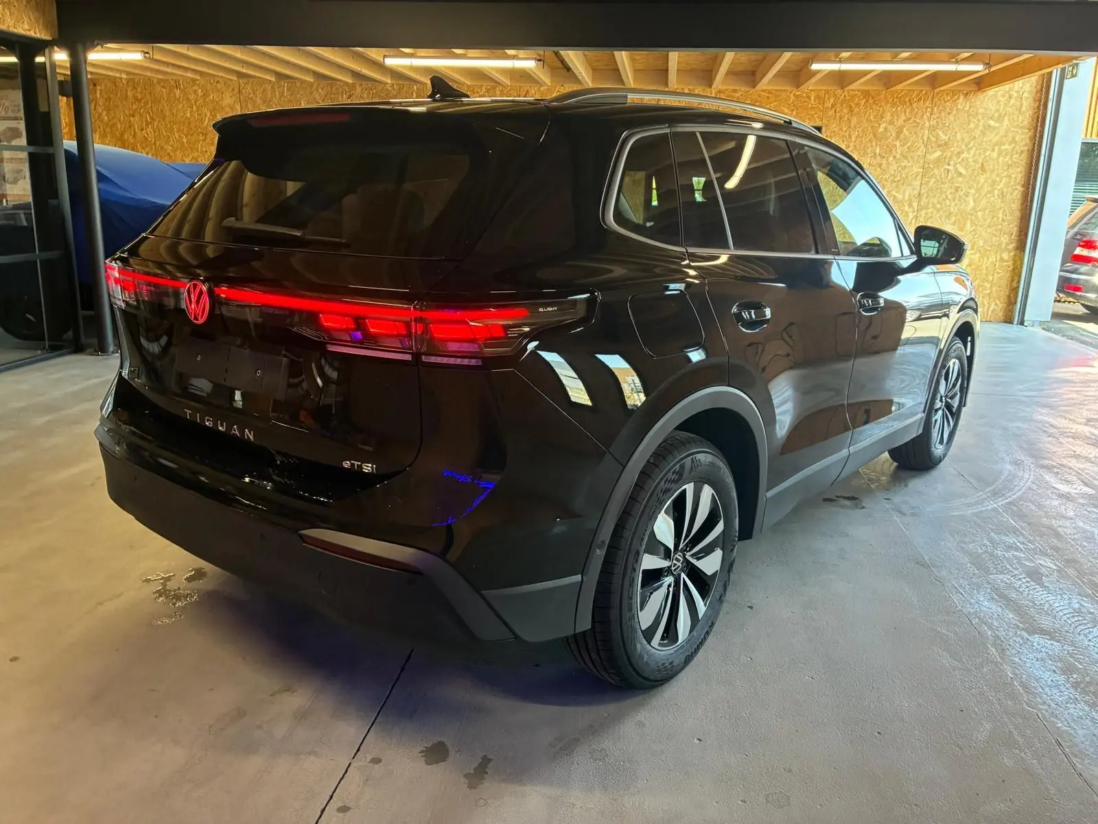 Vue 3/4 arrière droite du Volkswagen Tiguan noir Grenadilla Metal, avec feux arrière LED allumés dans un garage.