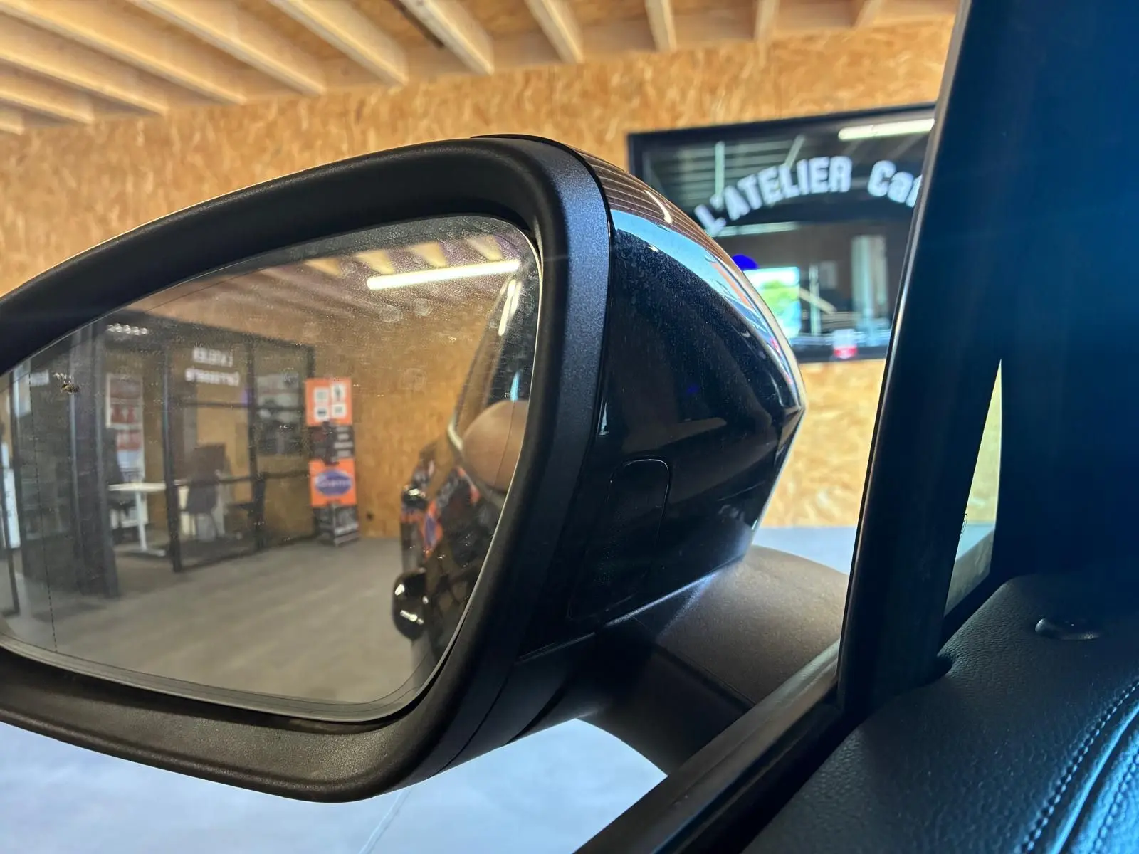 Rétroviseur extérieur côté gauche du Volkswagen Tiguan noir Grenadilla, reflet de l’intérieur d’un atelier.