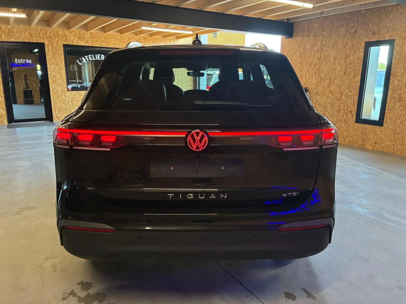 Vue arrière d'un Volkswagen Tiguan noir Grenadilla avec feux arrière LED allumés dans un garage.