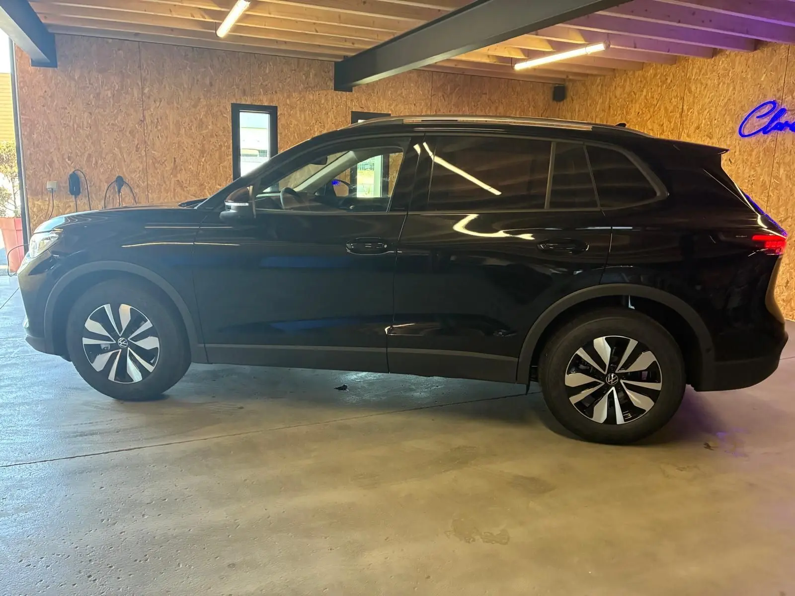 Volkswagen Tiguan 1.5 TSI noir grenadilla métal vu de profil côté gauche en intérieur avec jantes bicolores.