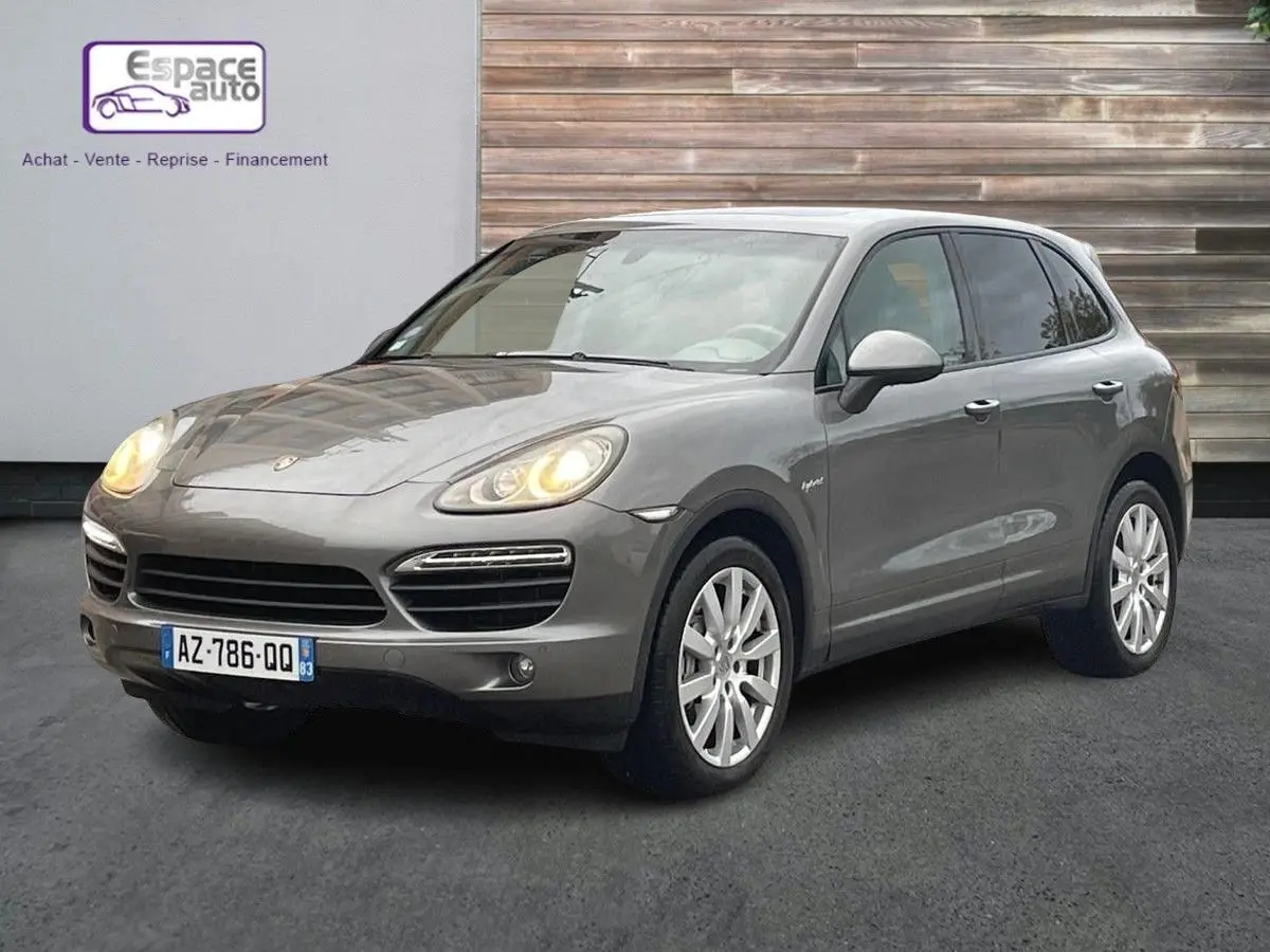 Porsche Cayenne S Hybrid gris vu en 3/4 avant droit avec phares allumés et jantes argentées.