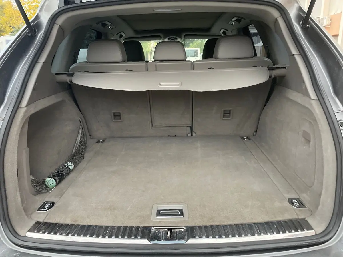 Coffre ouvert d'un Porsche Cayenne S Hybrid gris 2010, montrant un espace de chargement propre avec cache-bagages déployé.