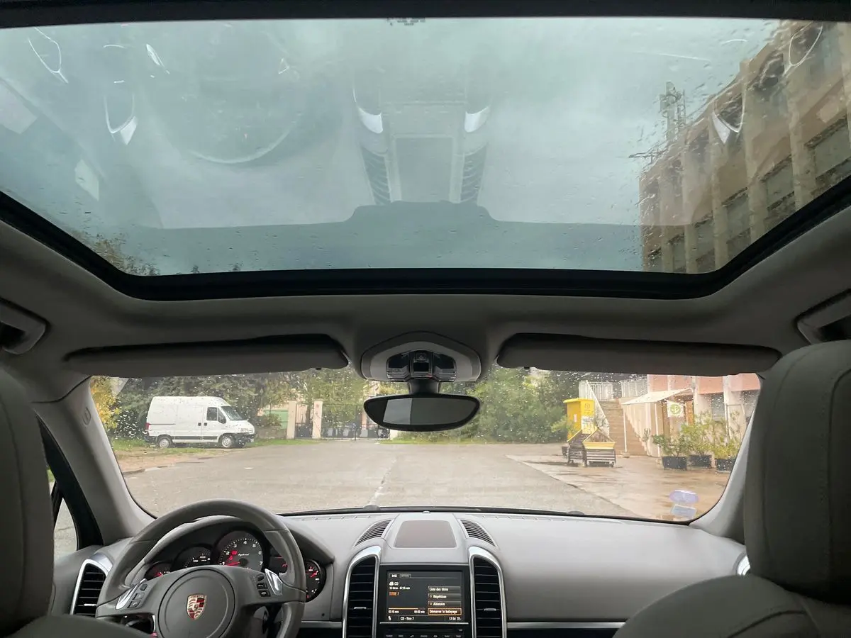 Vue intérieure du Porsche Cayenne S Hybrid 2010, montrant le tableau de bord, volant et toit panoramique sous la pluie.