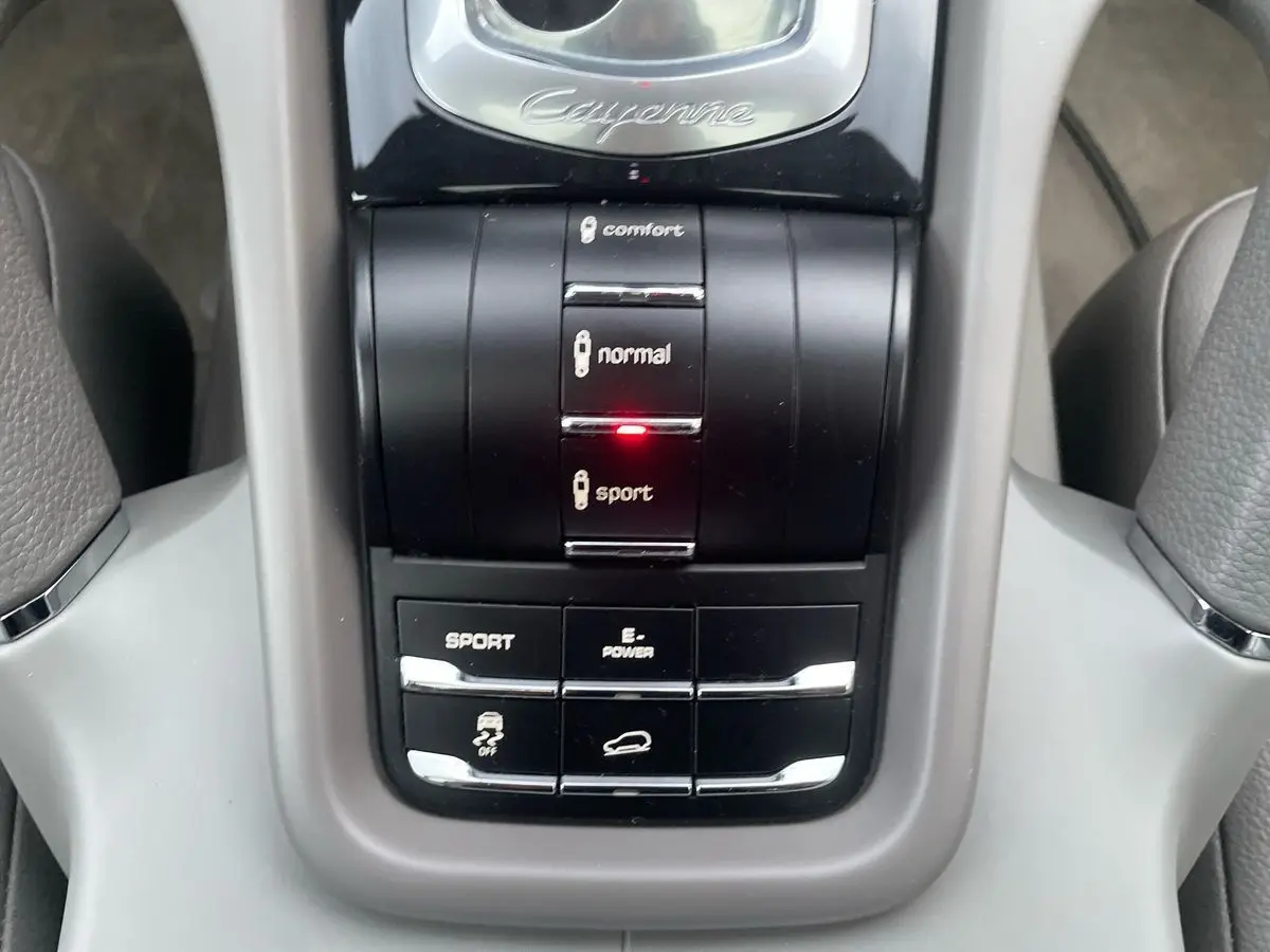 Gros plan sur la console centrale du Porsche Cayenne S Hybrid 2010 gris, avec mode sport activé et commandes de conduite.