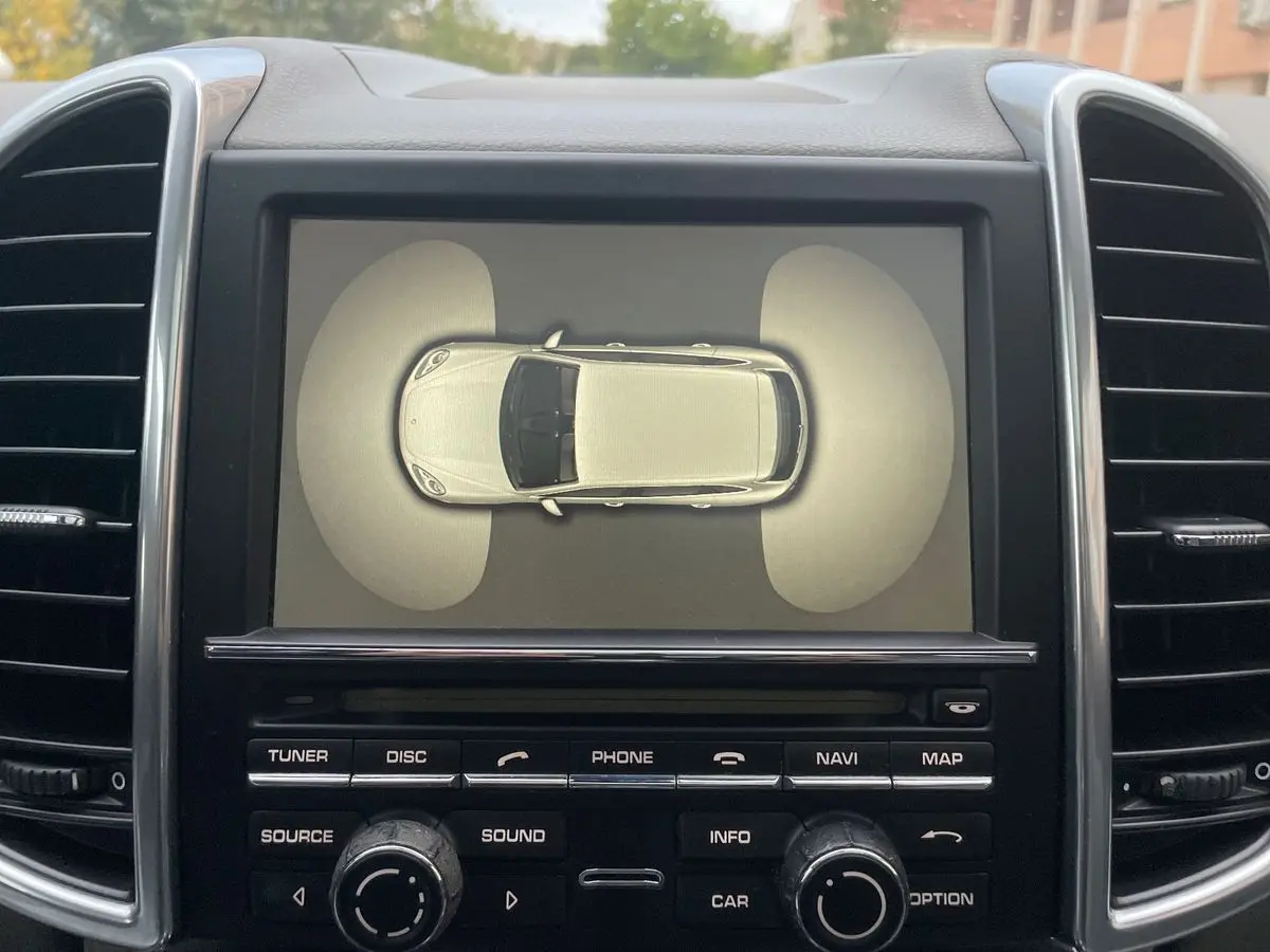 Écran central du Porsche Cayenne S Hybrid 2010 montrant une vue aérienne du véhicule gris avec capteurs avant et arrière activés.