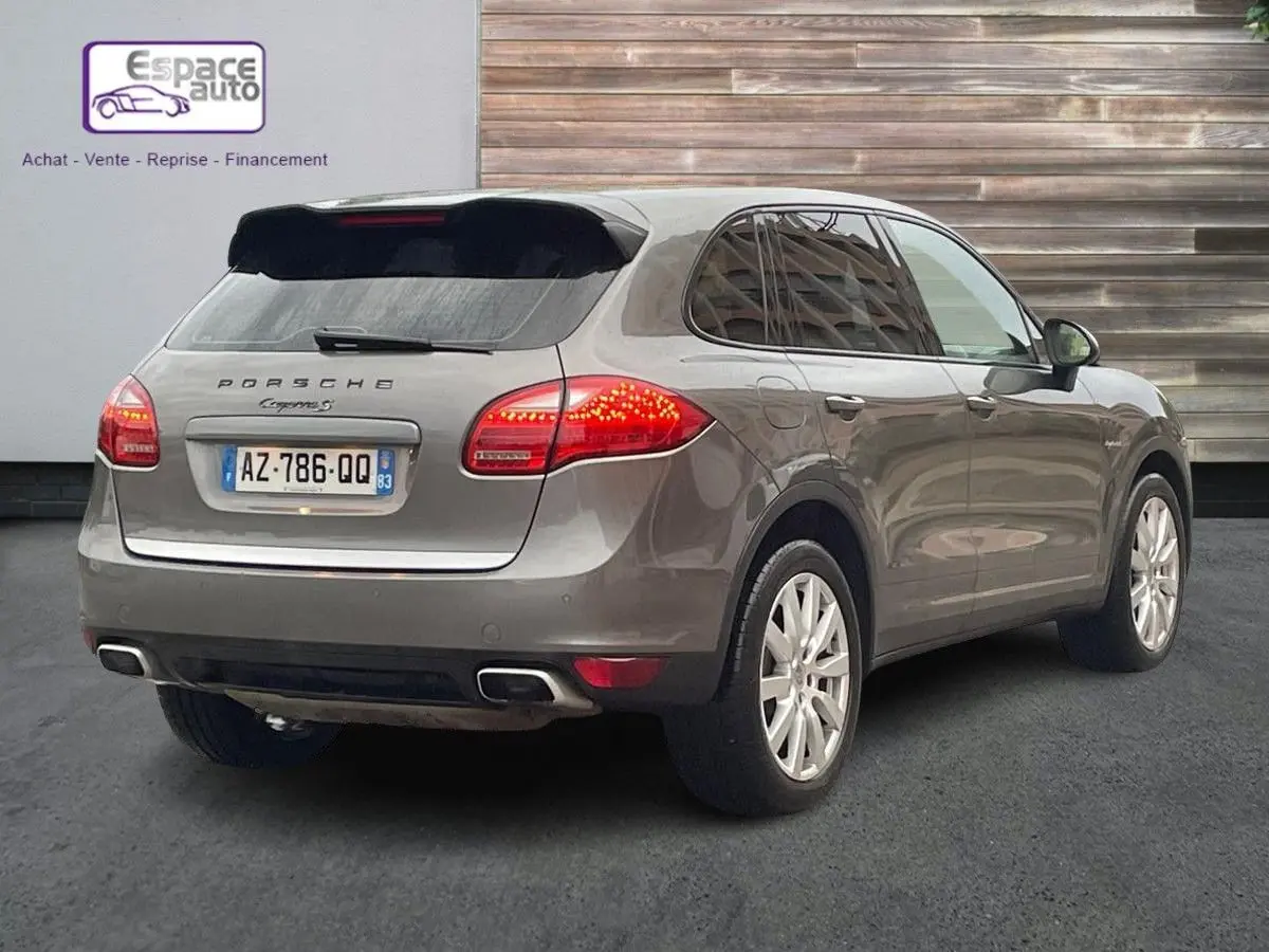 Vue 3/4 arrière droite d'un Porsche Cayenne S Hybrid gris 2010 avec feux arrière allumés et jantes argentées.