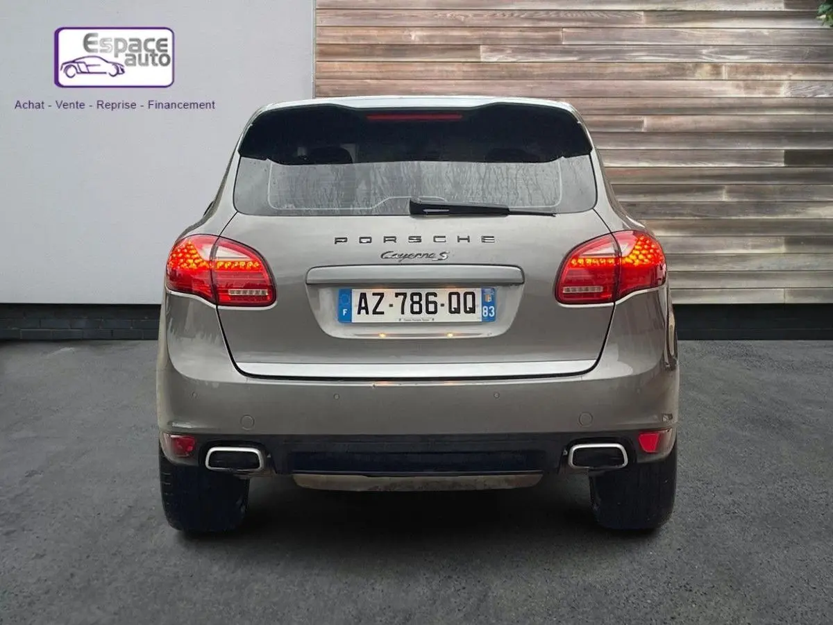 Vue arrière d'un Porsche Cayenne S Hybrid gris de 2010 avec feux allumés et double sortie d'échappement rectangulaire.