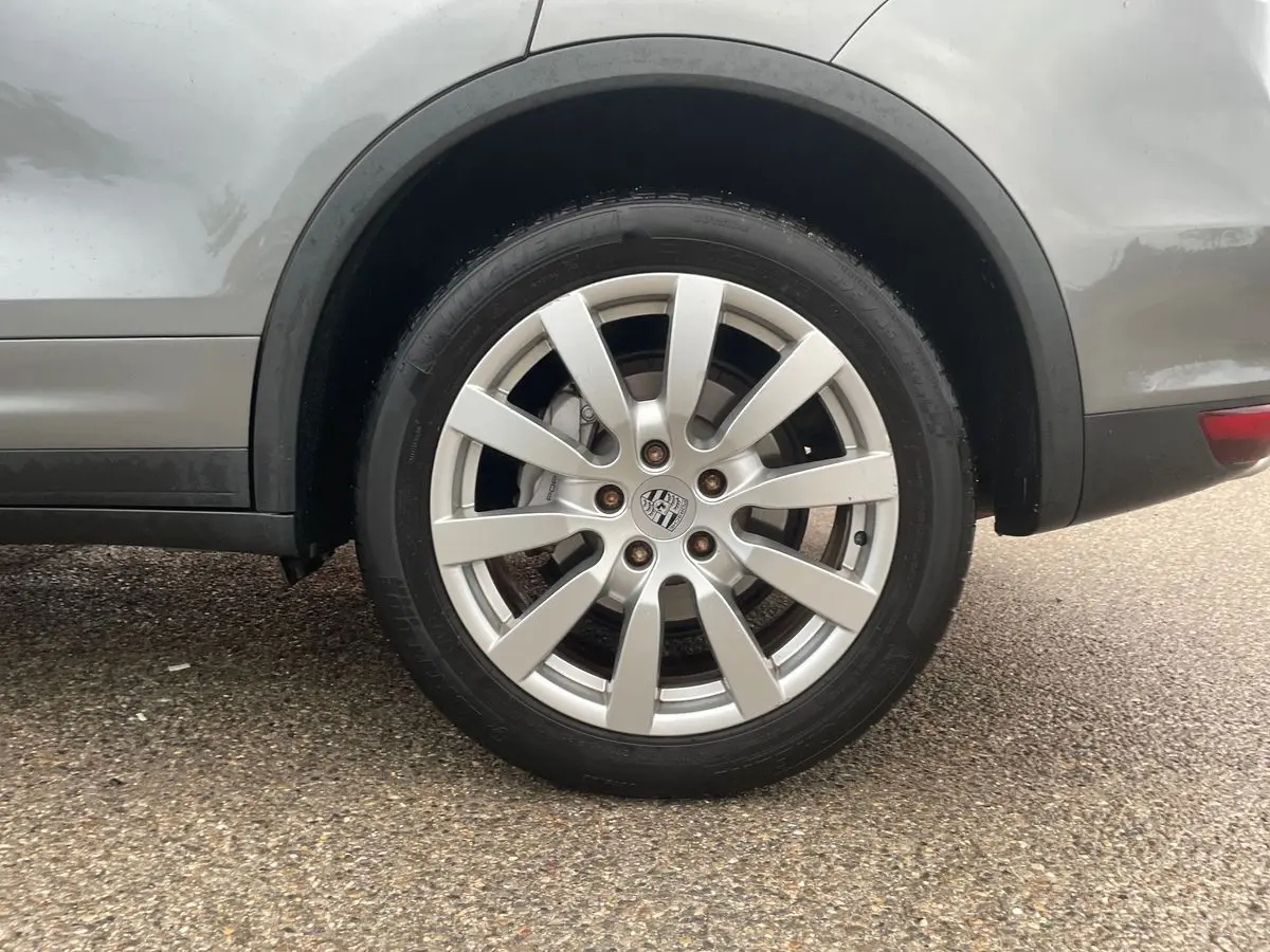 Gros plan sur la roue arrière droite d'un Porsche Cayenne S Hybrid gris 2010 avec jante alliage et logo Porsche central.