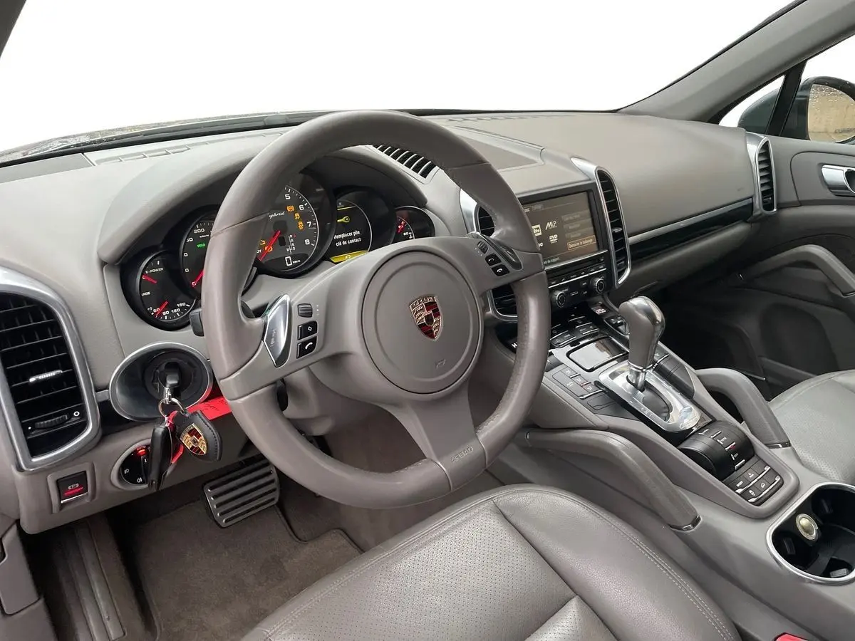 Intérieur gris clair du Porsche Cayenne S Hybrid 2010 vu côté conducteur, volant multifonction et console centrale avec levier automatique.