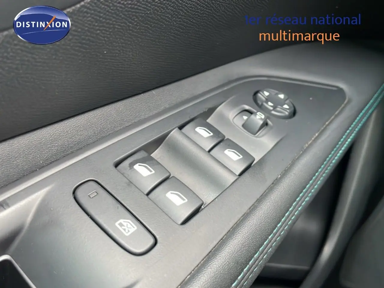 Gros plan sur les commandes de lève-vitres et rétroviseurs côté conducteur, garniture noire avec surpiqûres bleues.