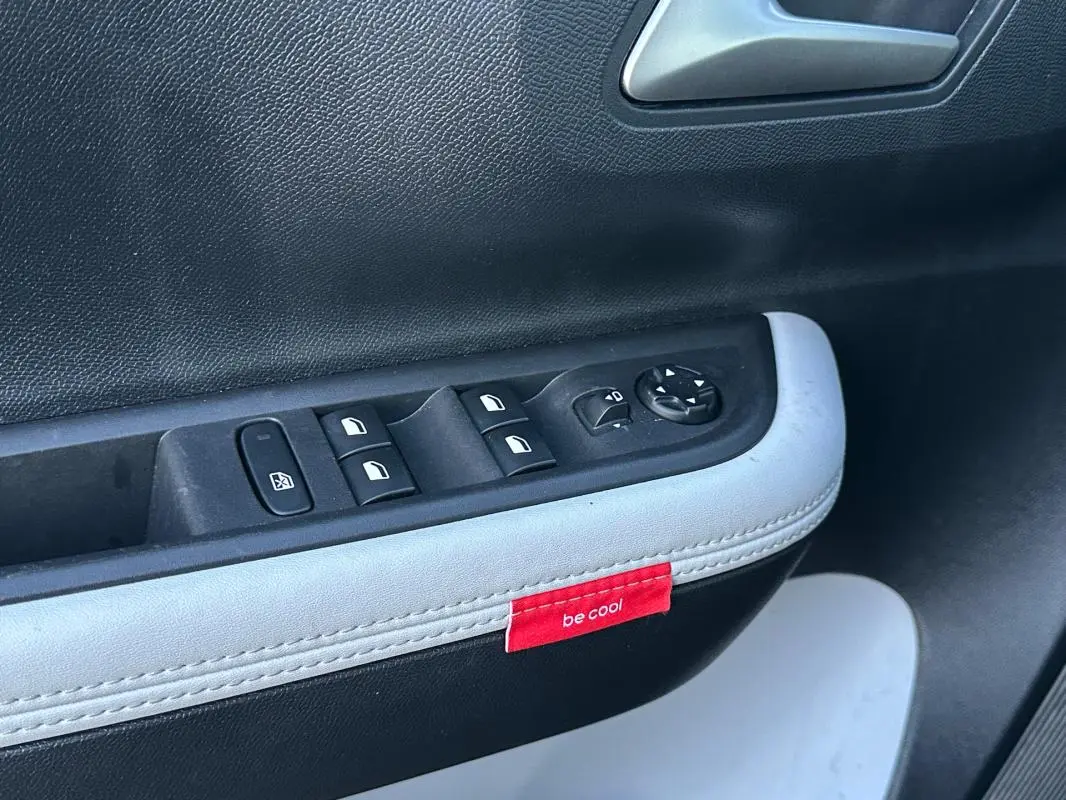 Gros plan sur la commande des vitres et rétroviseurs côté conducteur de la Citroën C3 noire avec étiquette rouge "be cool" sur la garniture.