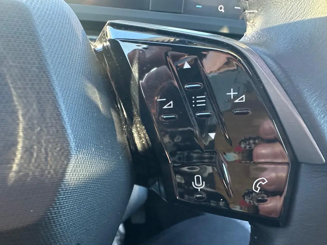 Gros plan sur les commandes au volant noir brillant du Peugeot 3008 blanc Hybrid 145 e-DCS6 Allure 2025.