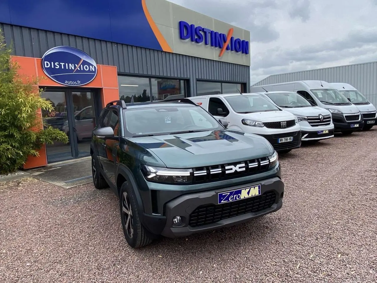 Dacia Duster 1.6 Hybrid 2025 vert INC en 3/4 avant droit, avec calandre moderne et plaques Zero KM visibles.