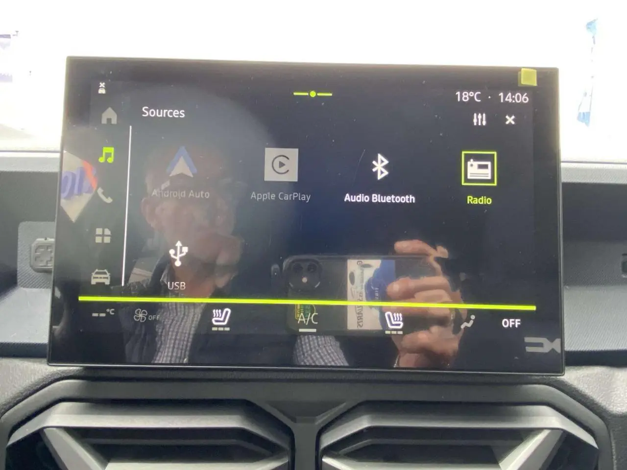 Écran tactile central du Dacia Duster 2025 affichant les options multimédia et climatisation, avec reflet partiel.