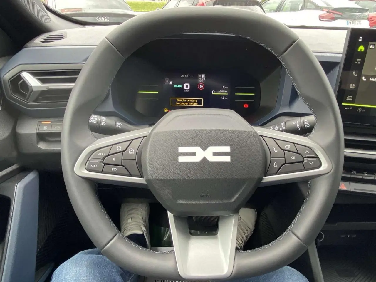 Vue intérieure centrée sur le volant noir du Dacia Duster 1.6 Hybrid 2025 avec tableau de bord digital allumé.