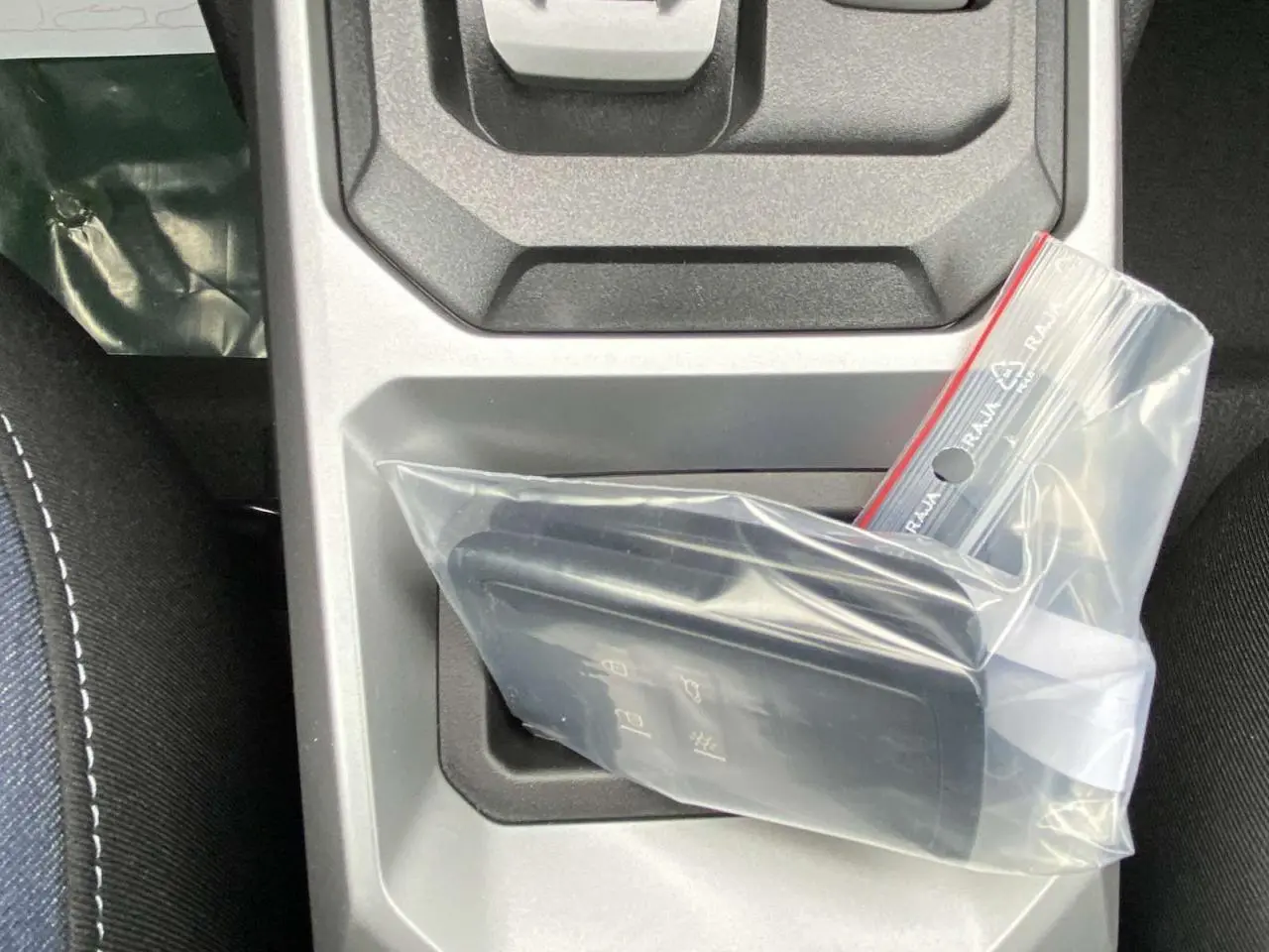 Gros plan sur la clé de la Dacia Duster 1.6 Hybrid 2025 dans un sac plastique, posée sur la console centrale grise.