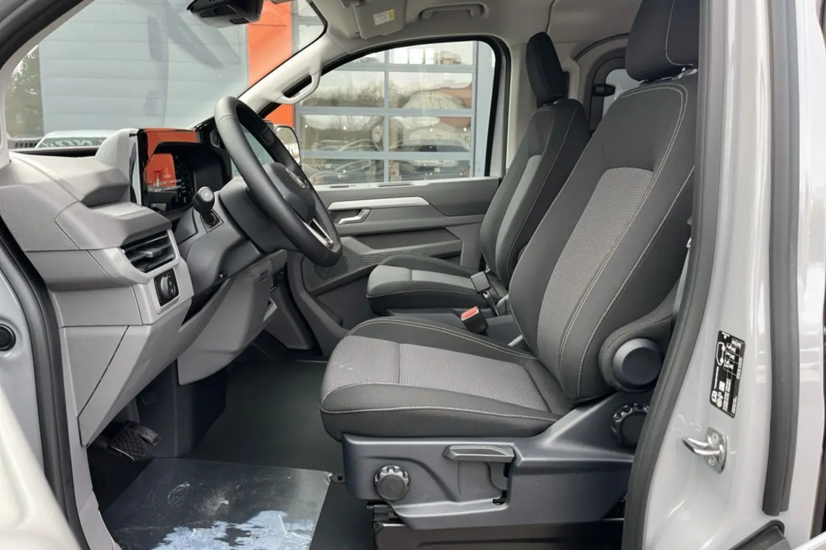 Vue intérieure côté conducteur du Volkswagen Transporter TDI 170 DSG ProCab L1 gris Stone, sièges tissu noir et tableau de bord moderne.