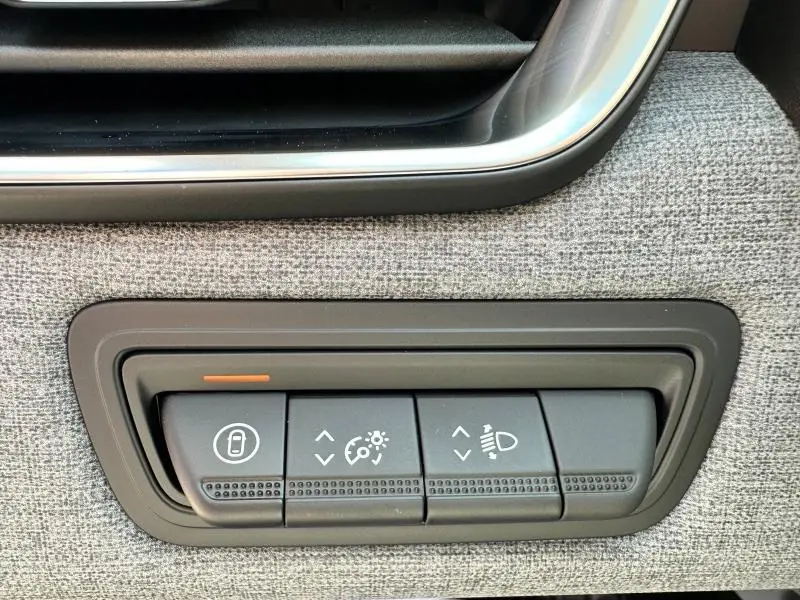 Gros plan sur les commandes de réglage des feux et verrouillage sur la porte côté conducteur en tissu gris de la Renault Clio Blanc Glacier 2025.