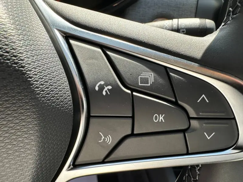Gros plan sur les commandes multifonctions noires du volant côté gauche de la Renault Clio blanche Glacier 2025.