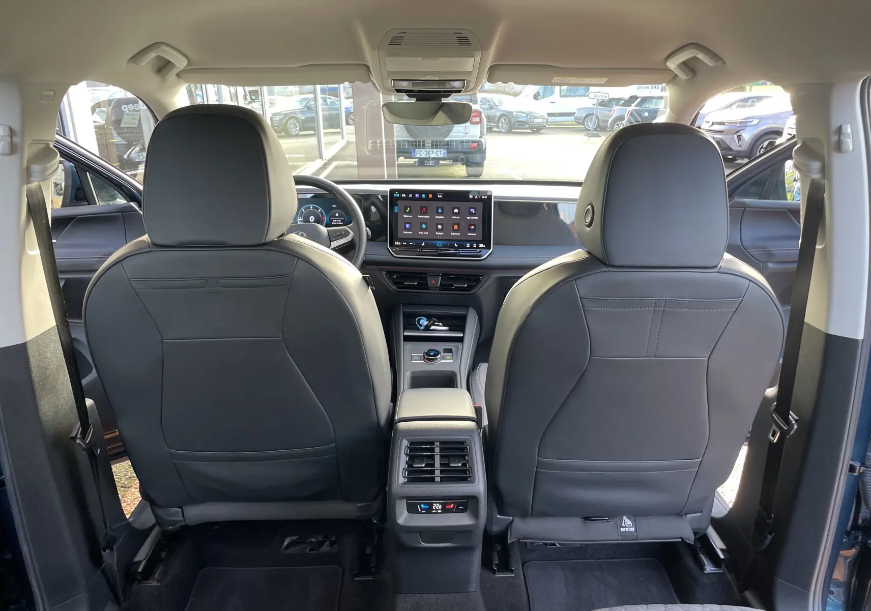 Vue intérieure arrière du Volkswagen Tiguan 2024 en Nightshade Blue, montrant les sièges avant en cuir noir et l'écran tactile central.