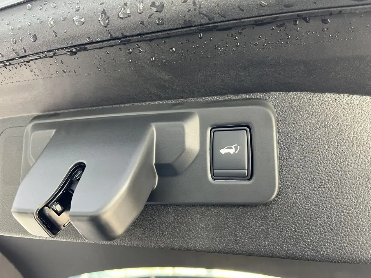 Gros plan sur la poignée intérieure de coffre avec bouton d’ouverture, sur Renault Austral gris schiste 2025.