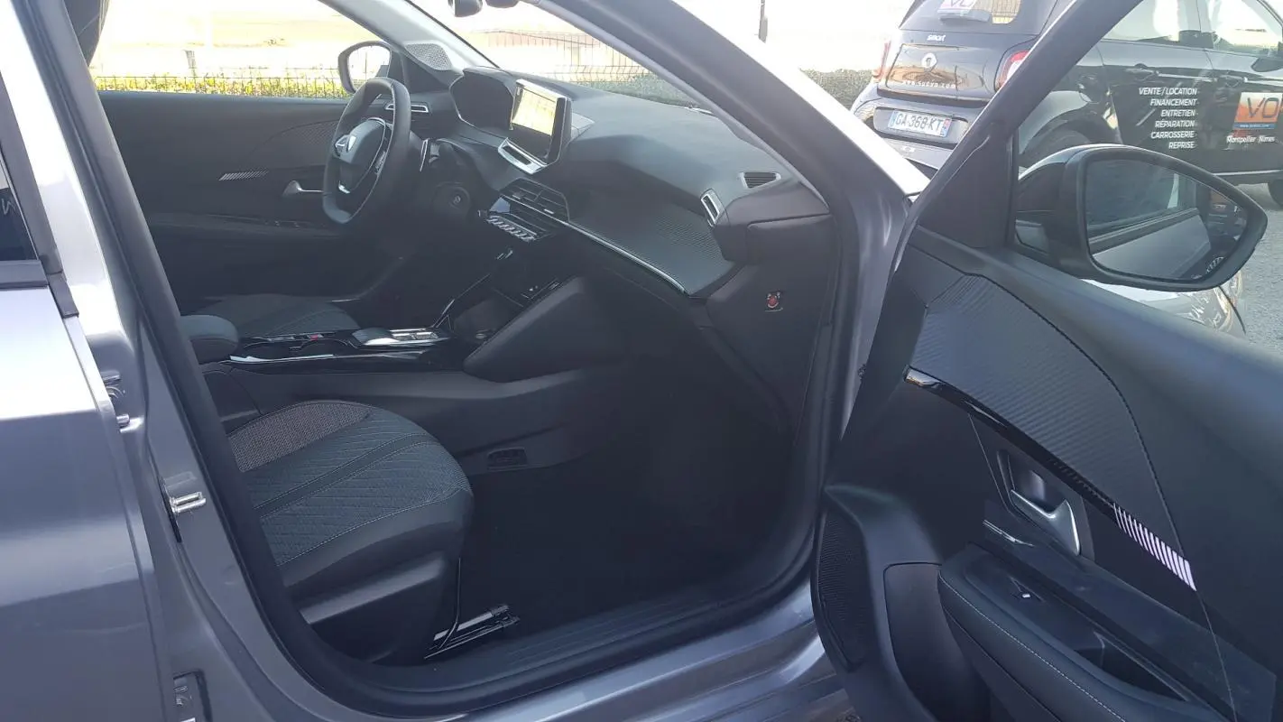 Vue intérieure côté conducteur d'une Peugeot 208 gris 2025, mettant en valeur le tableau de bord et l'écran tactile.
