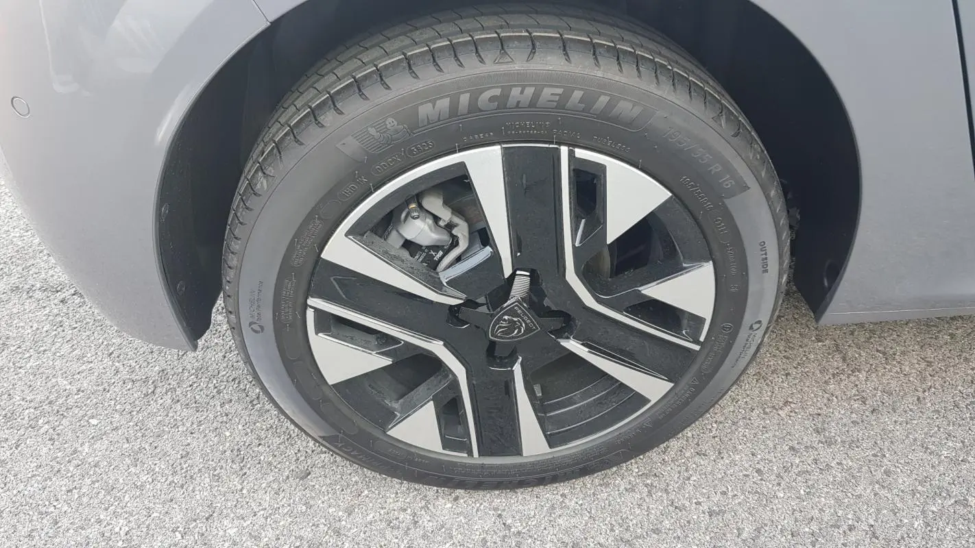 Gros plan sur la roue avant droite gris métallisé d'une Peugeot 208 Hybrid 110 e-DCS6 Allure avec jante alliage noire et argent.