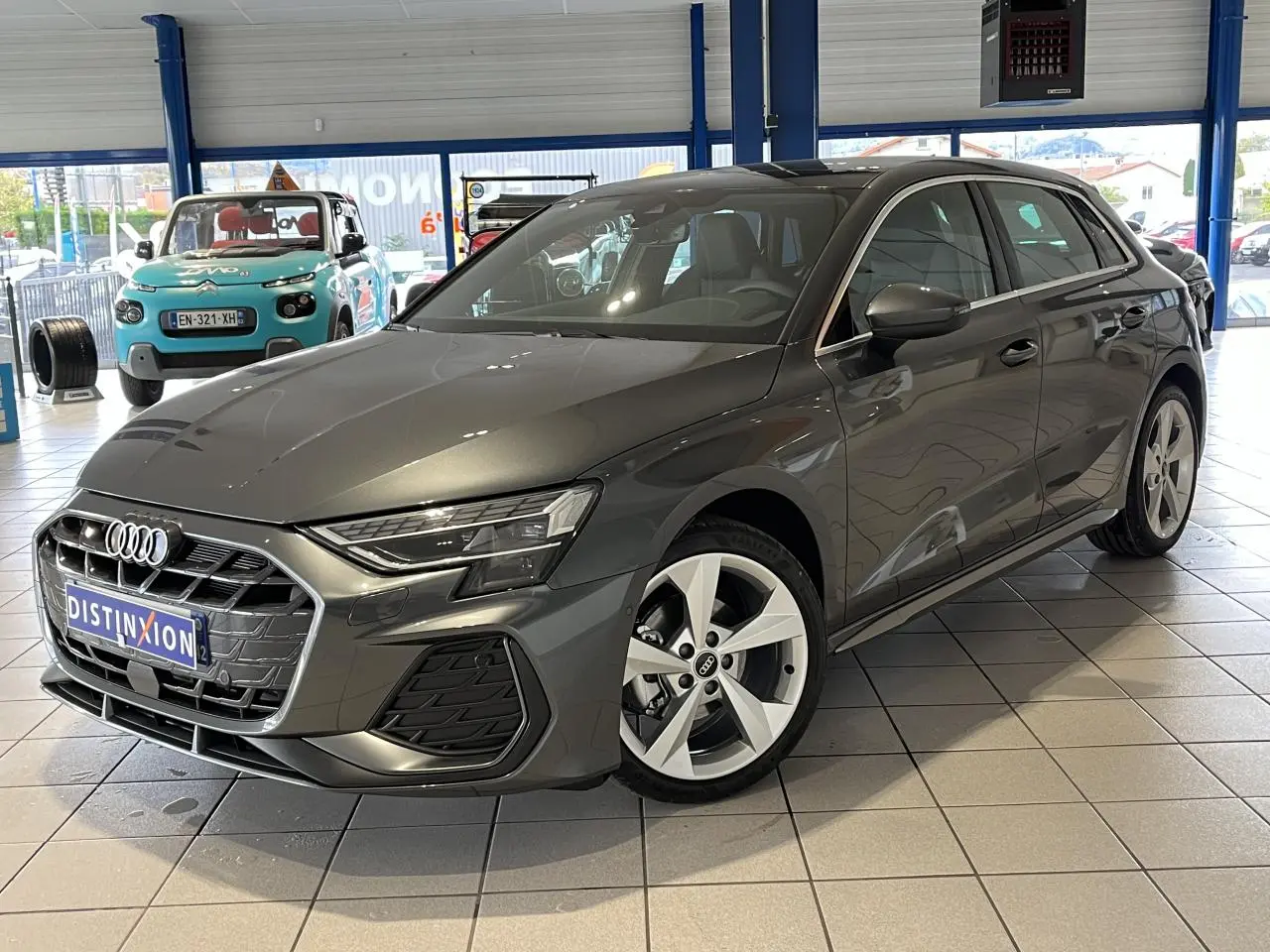Audi A3 Sportback gris en 3/4 avant droit, avec jantes alliage 5 branches et toit ouvrant panoramique visible en showroom.