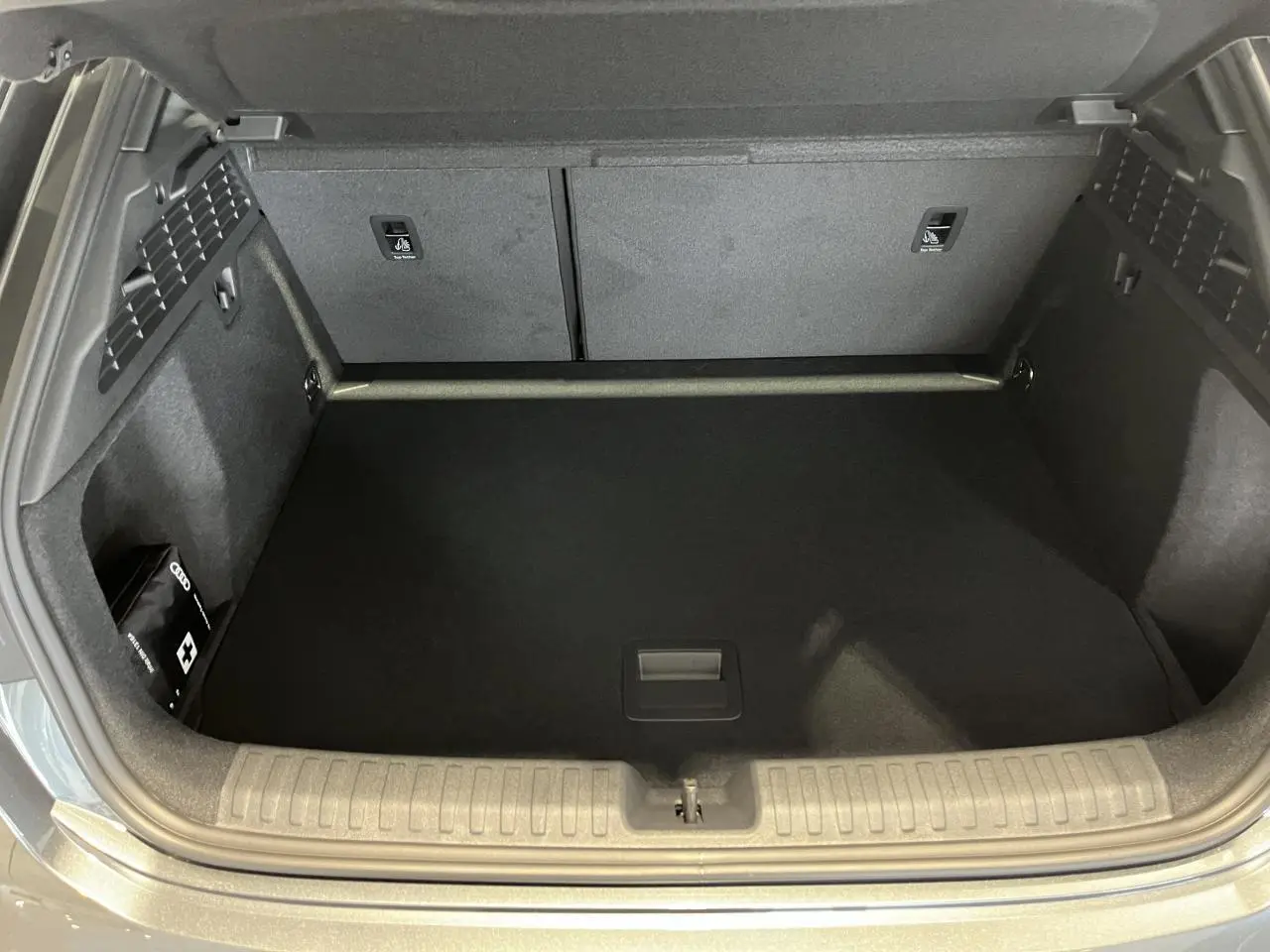 Coffre ouvert d’Audi A3 Sportback gris, vue de dessus montrant l’espace de chargement et une trousse de secours à gauche.