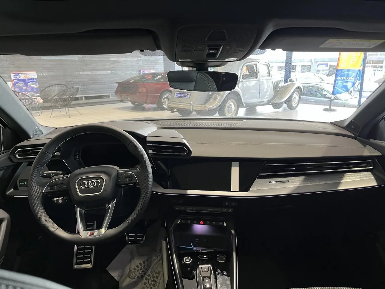 Vue intérieure avant de l'Audi A3 Sportback 2025 gris, tableau de bord moderne avec volant sport multifonctions et écran tactile central.