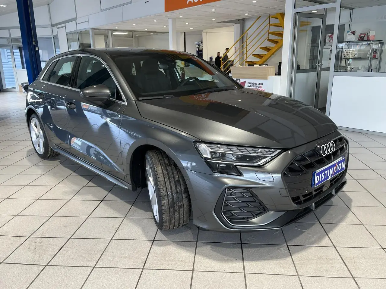 Audi A3 Sportback gris métallisé vue 3/4 avant en intérieur avec calandre noire et jantes 5 branches en Y.