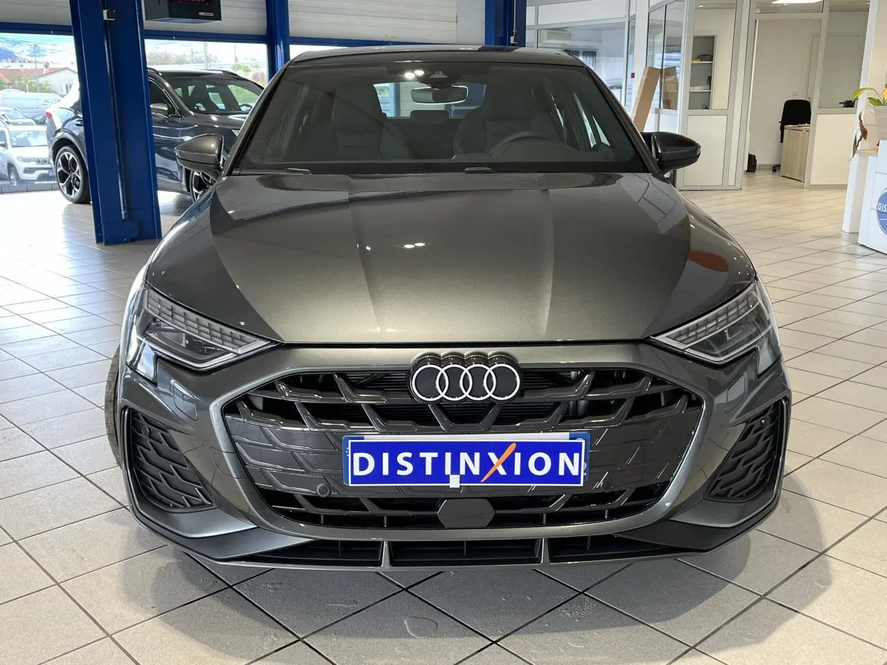 Vue frontale d’une Audi A3 Sportback gris métallisé 2025 avec calandre S line et phares LED dynamiques en showroom.