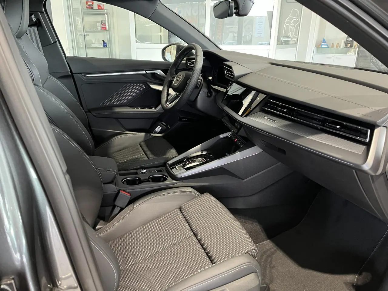 Intérieur noir de l'Audi A3 Sportback 2025 vu côté passager, avec tableau de bord moderne et volant cuir sport.