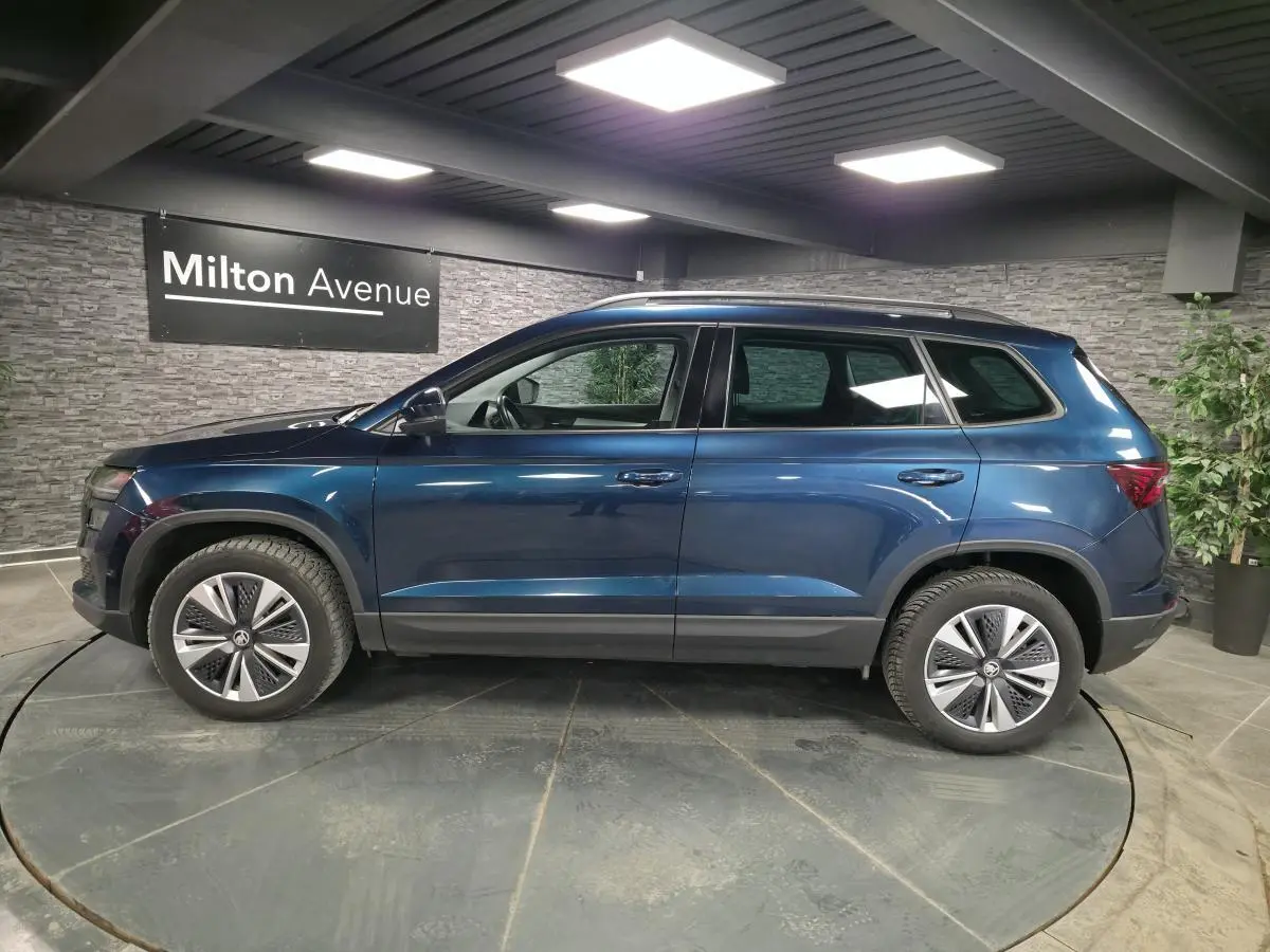 Vue latérale droite d'un Skoda Karoq bleu métallisé 2024 en showroom avec jantes alliage 17 pouces.