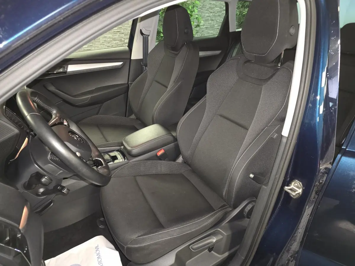 Vue intérieure côté conducteur du Skoda Karoq bleu 2024, sièges tissu noir avec accoudoir central et volant cuir.